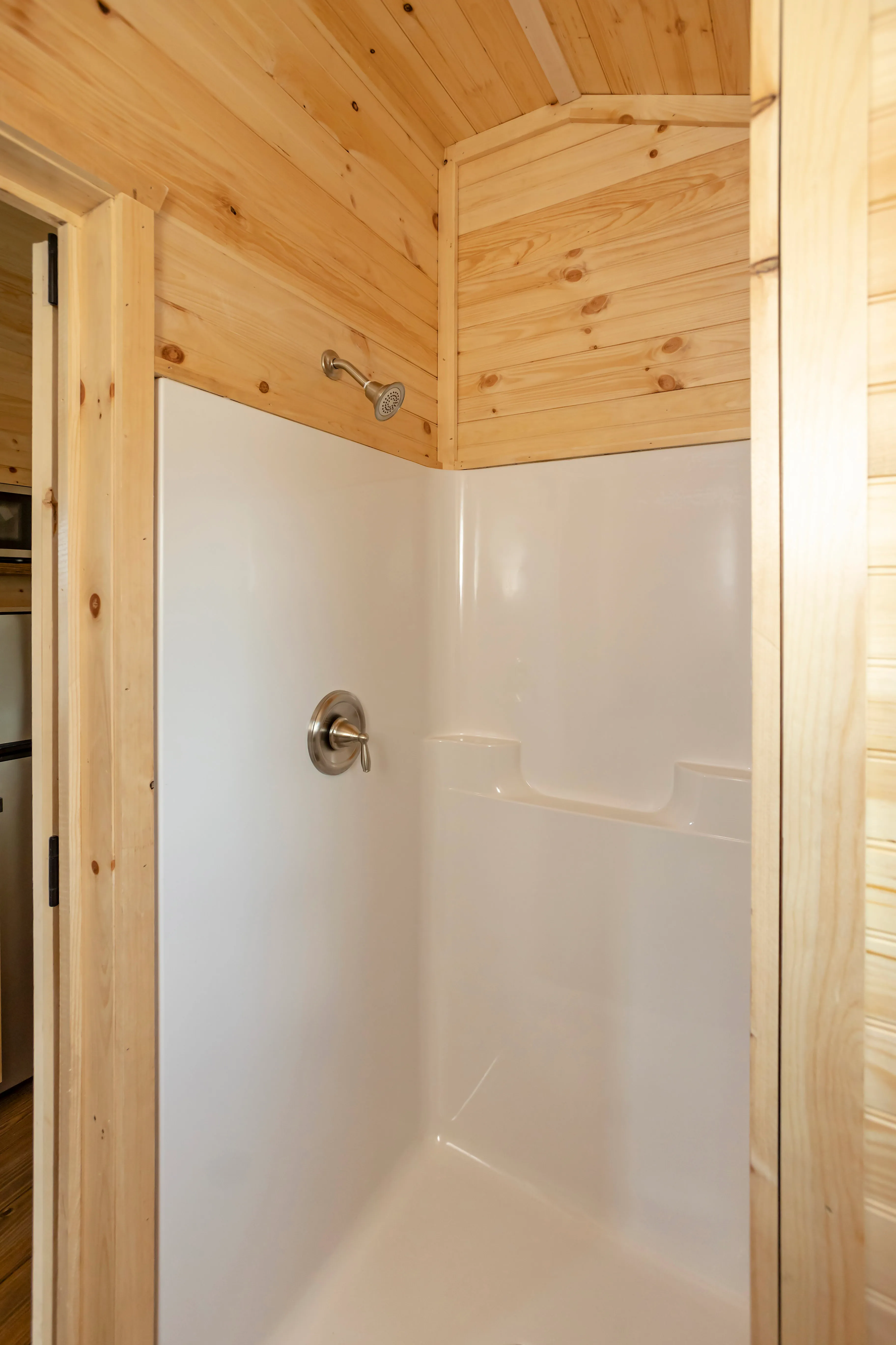 Shower stall with white walls and chrome fixtures in a bathroom with light wood paneling.