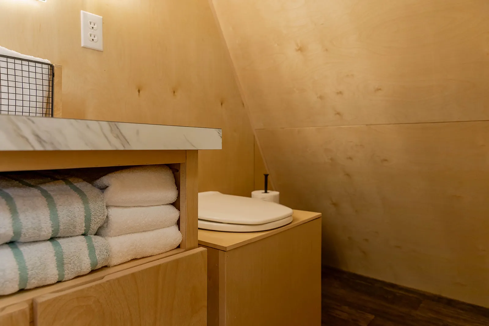 A small bathroom with light wood walls, a counter with stacked towels, a toilet with a closed lid.