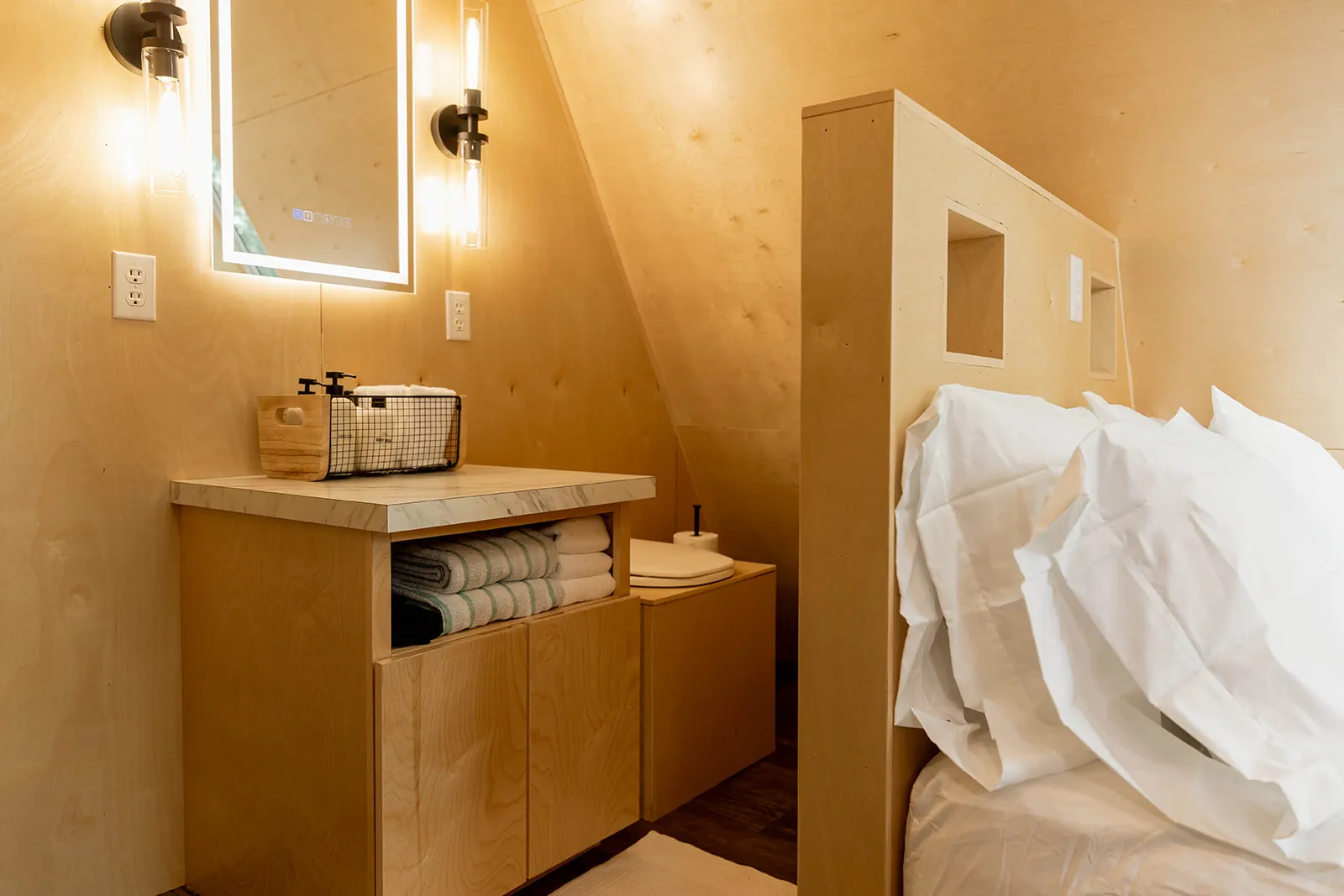 A modern minimalist bathroom with light wood walls, an open vanity with folded towels, a mirror, and toilet.
