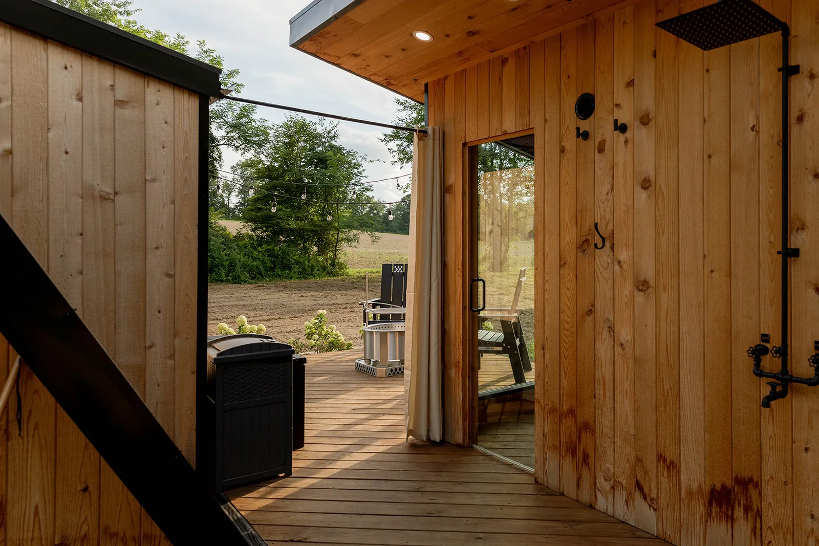 Wooden deck area with outdoor seating, next to the cabin and sauna with wooden outdoor shower area with a rain shower head.