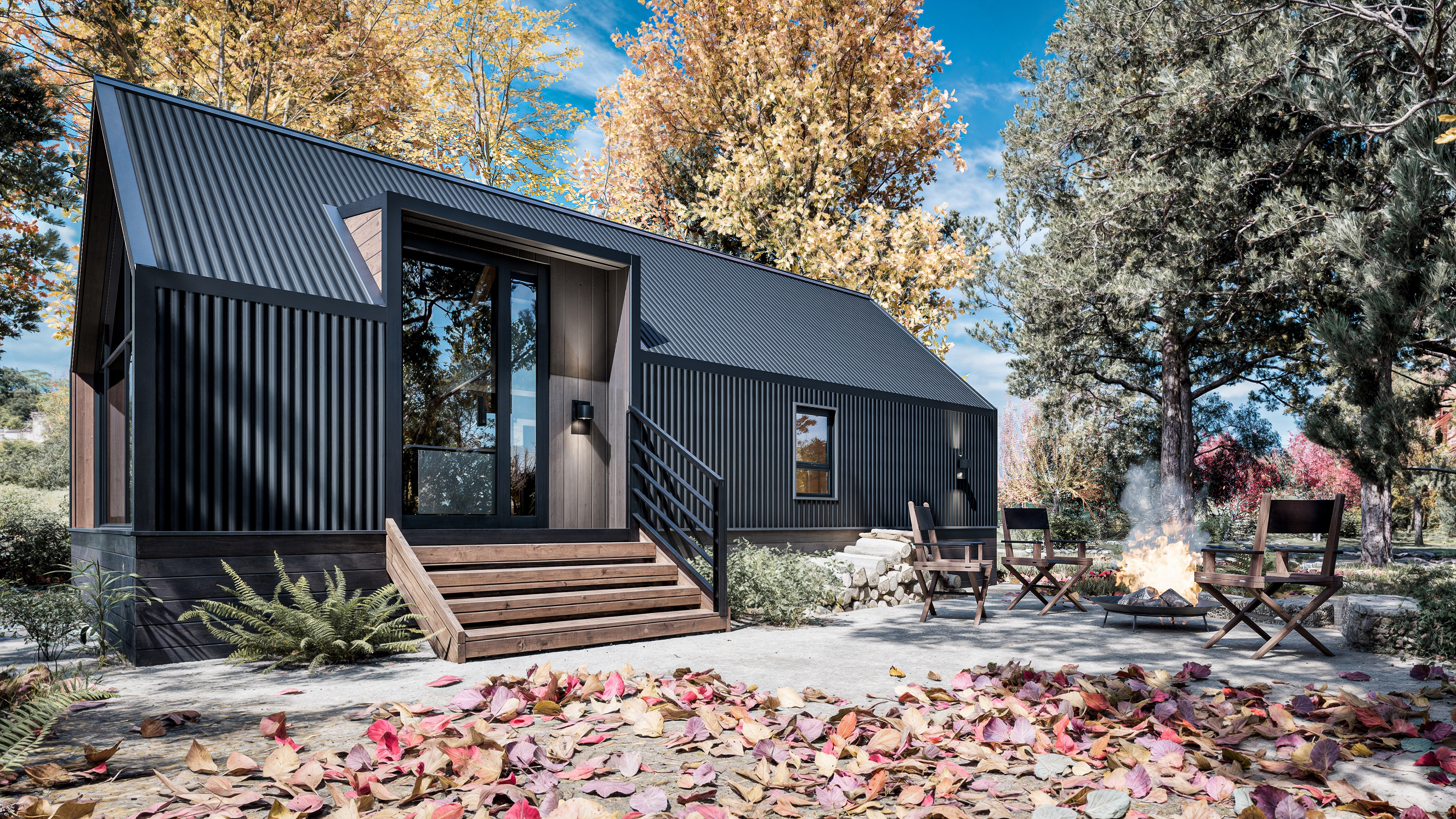 Modern black tiny house with wooden steps, surrounded by autumn trees. Chairs and a fire pit are set up on a leaf-covered patio in front of the house.