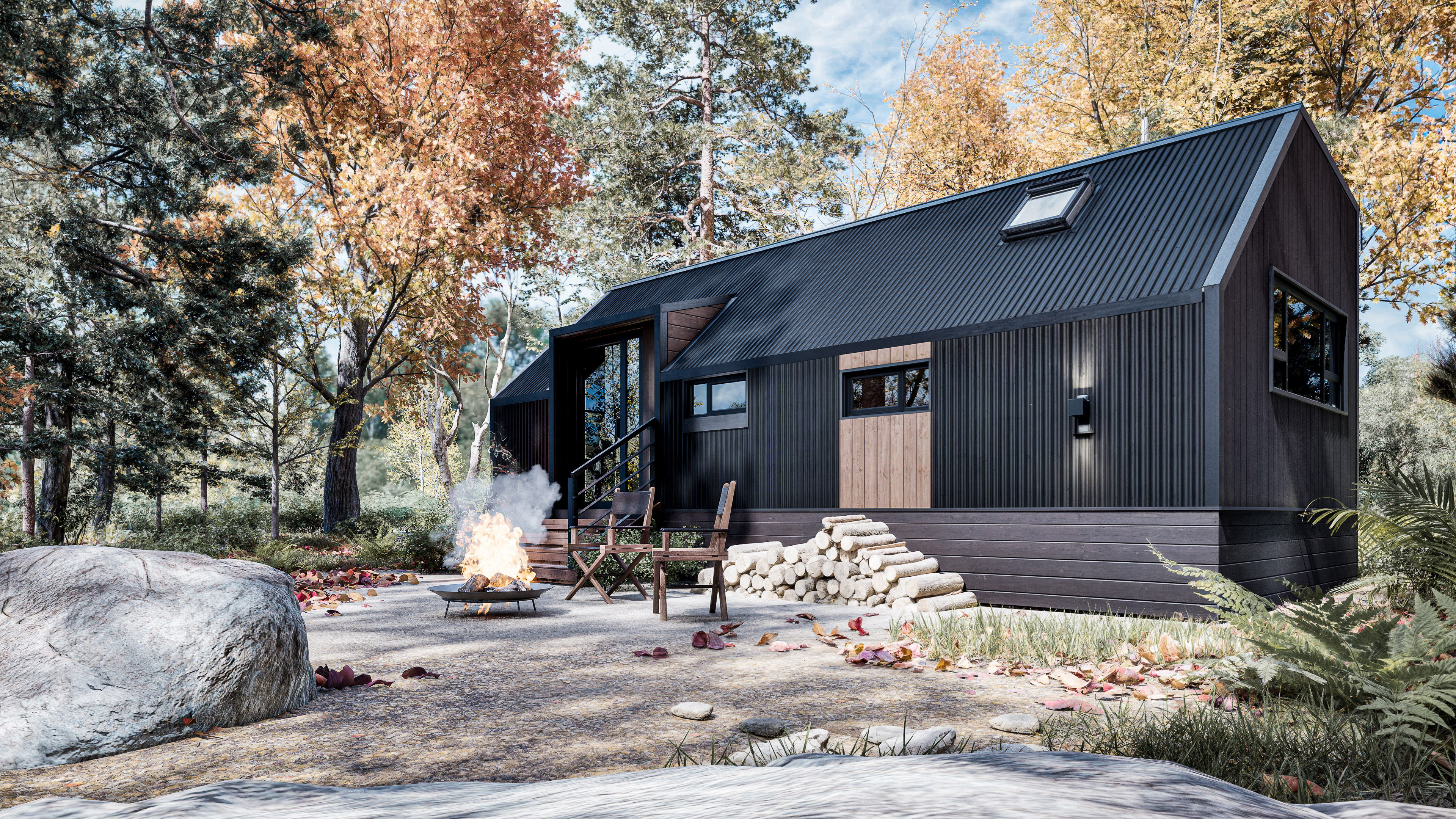 A modern black tiny house with stacked firewood and a fire pit with chairs outside, surrounded by autumn trees and fallen leaves.