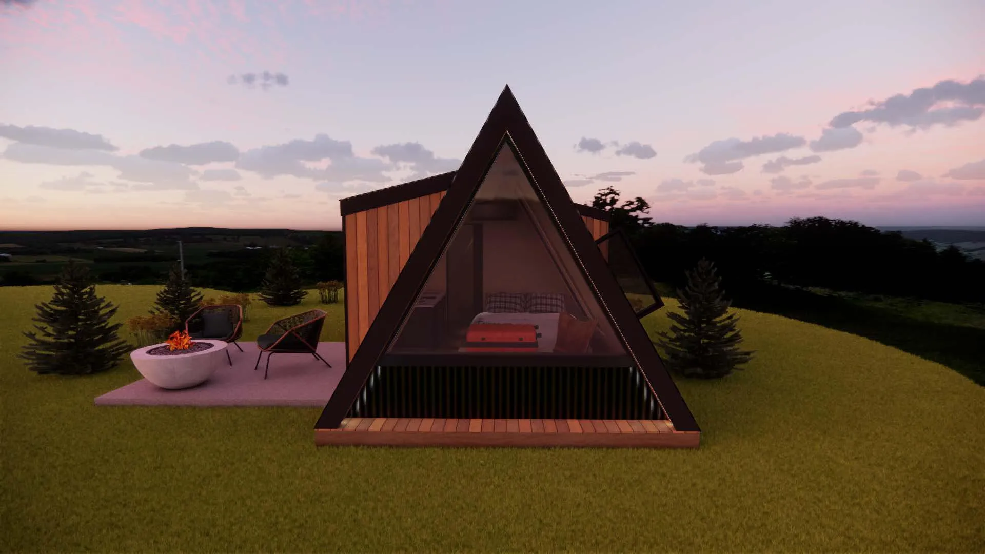 A-frame cabin with a glass front, bed visible inside, next to a patio with two chairs and a fire pit, set on grass with trees and hills in the background at sunset.