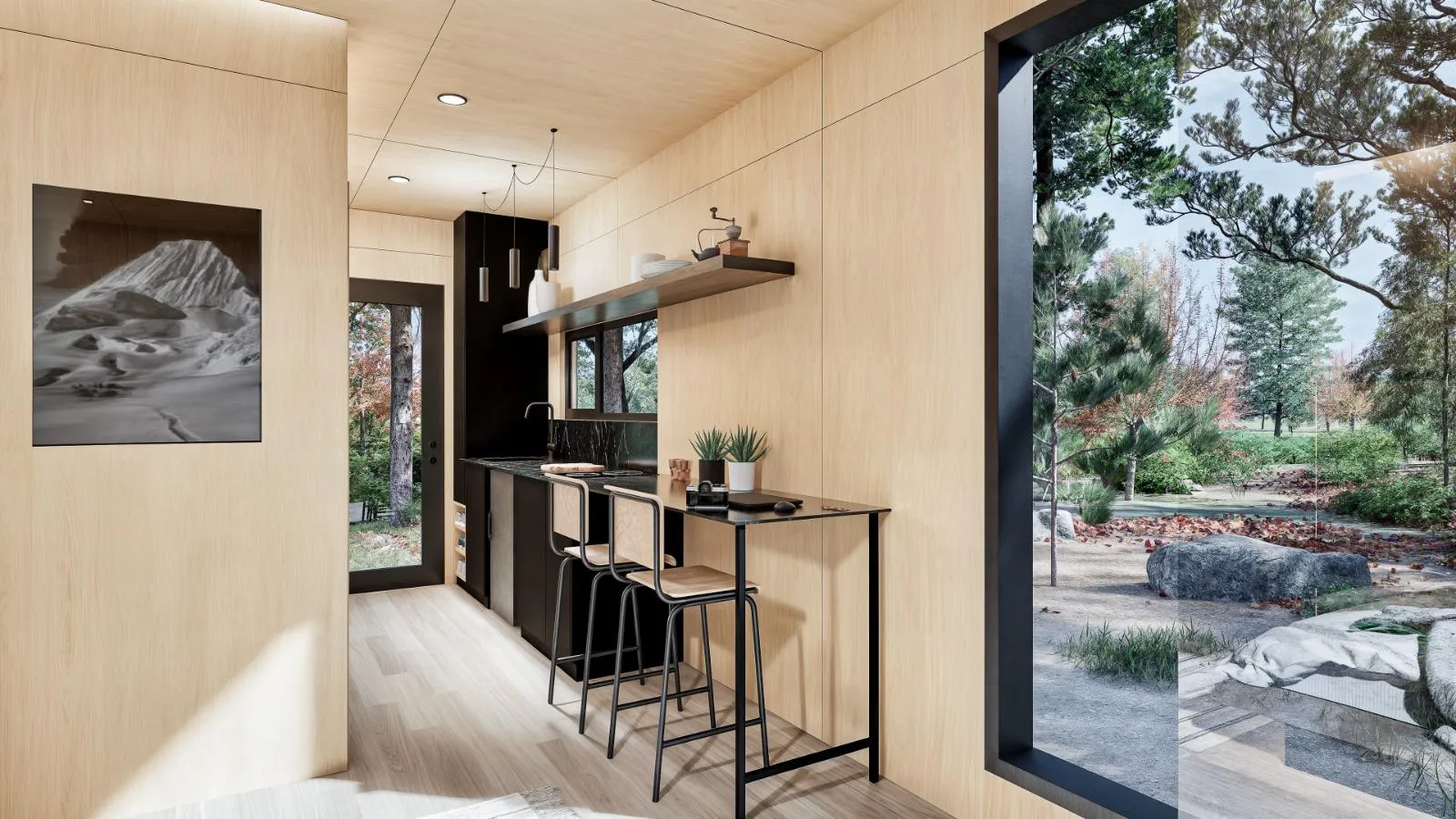 Interior of a modern cabin with light wood walls, a kitchenette, bar seating, large windows, and a view of trees and rocks outside.