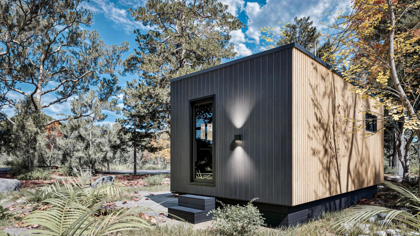 A small, modern wooden cabin with vertical siding and a single window, situated in a forested area.