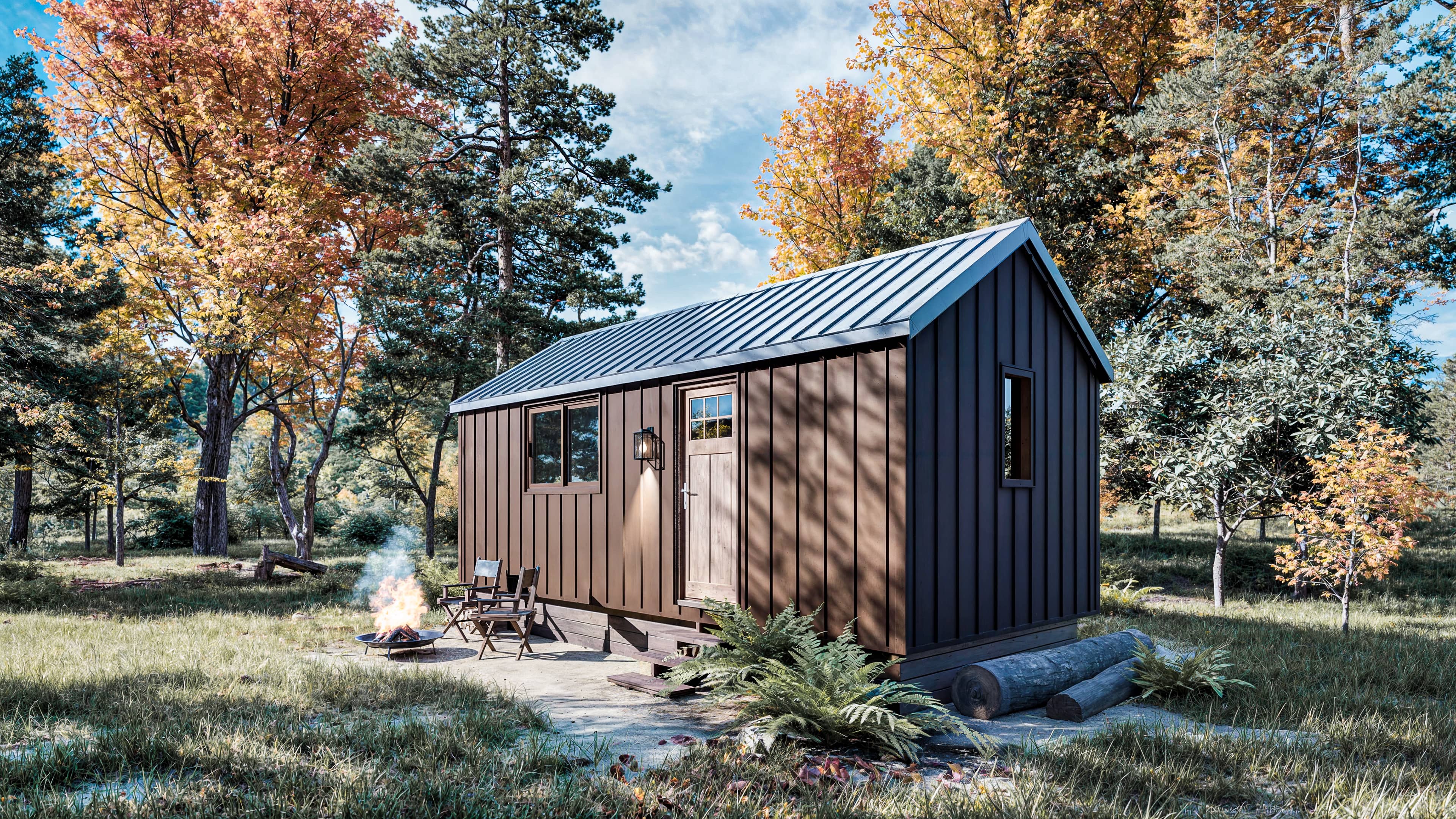 Small brown cabin with a metal roof sits in a forest clearing. Two chairs and a fire pit are in front, and autumn trees with colorful leaves surround the scene.