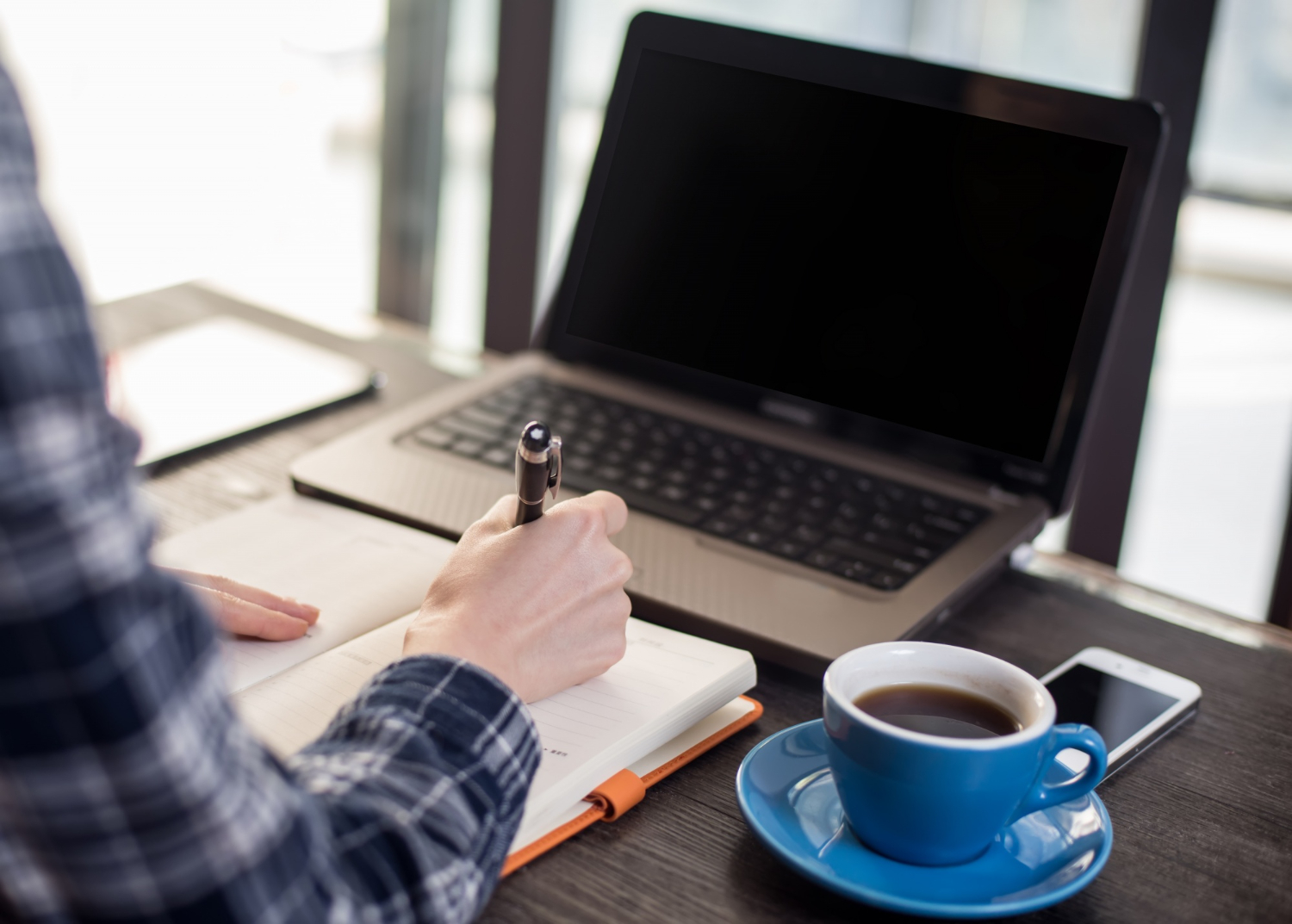 A close-up of someone writing interview notes on a notepad next to a laptop 