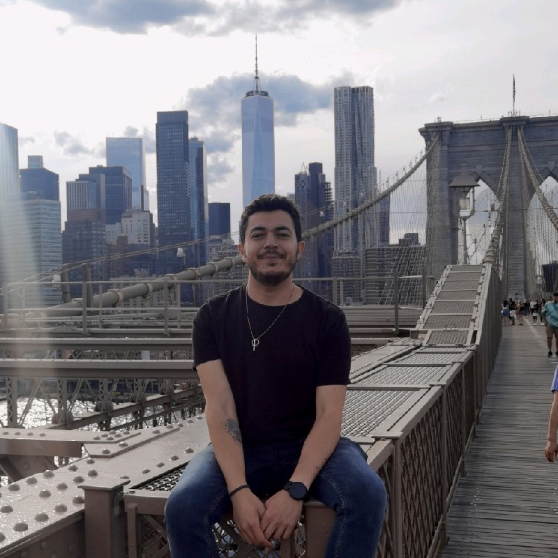 Žena s hnědými vlasy se usmívá venku, v pozadí jsou stromy a žluté listí.