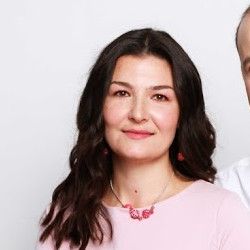 Žena s hnědými vlasy se usmívá venku, v pozadí jsou stromy a žluté listí.