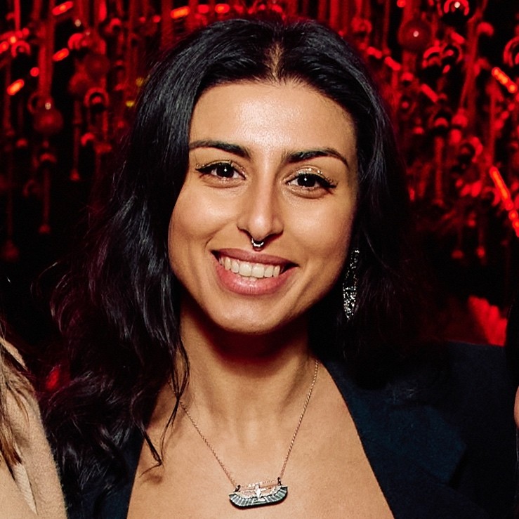 Žena s hnědými vlasy se usmívá venku, v pozadí jsou stromy a žluté listí.