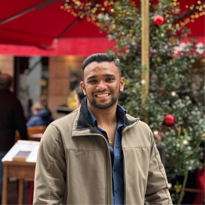 Žena s hnědými vlasy se usmívá venku, v pozadí jsou stromy a žluté listí.