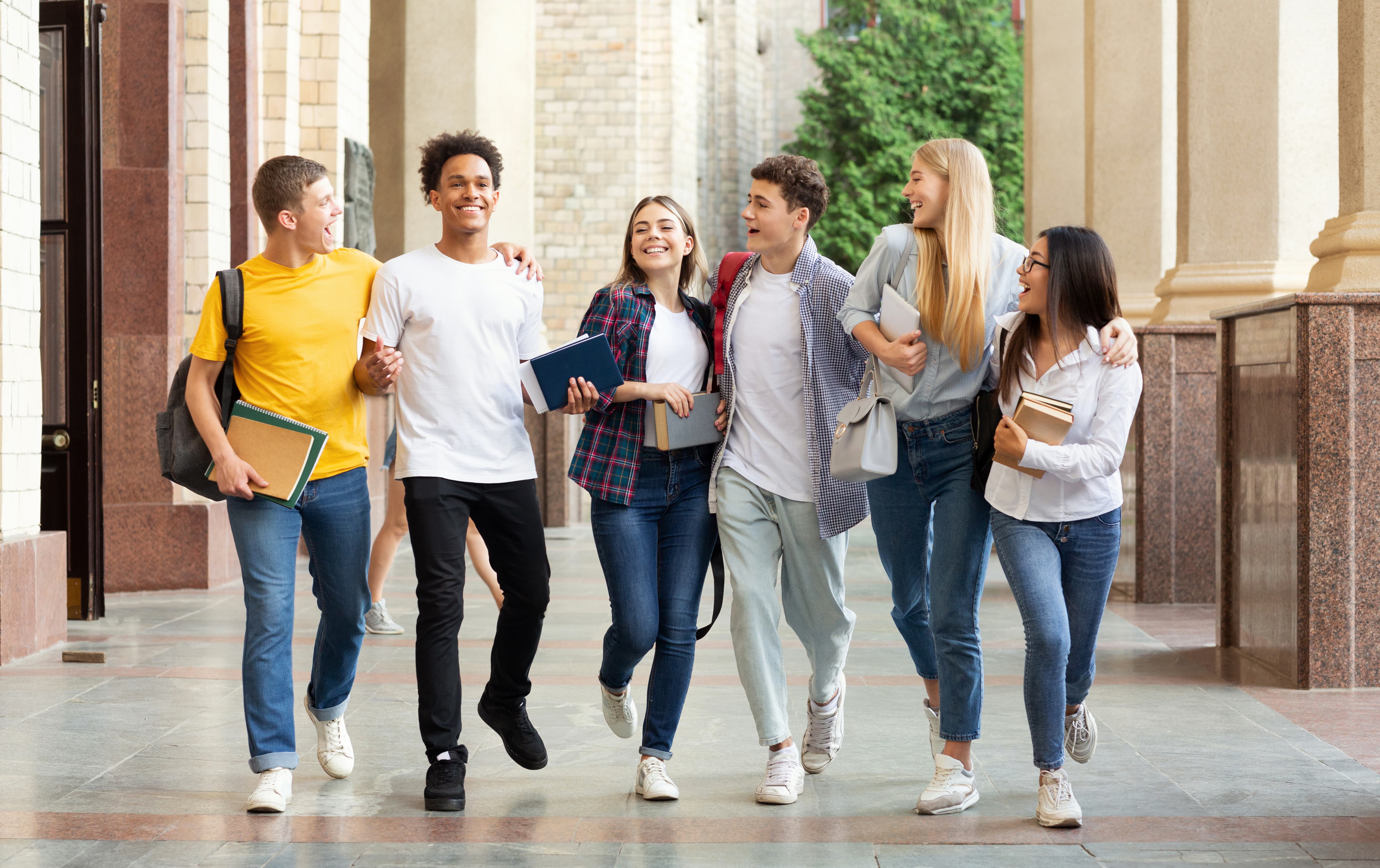Skupina šesti studentů jde chodbou a směje se, každý drží knihy a batoh.