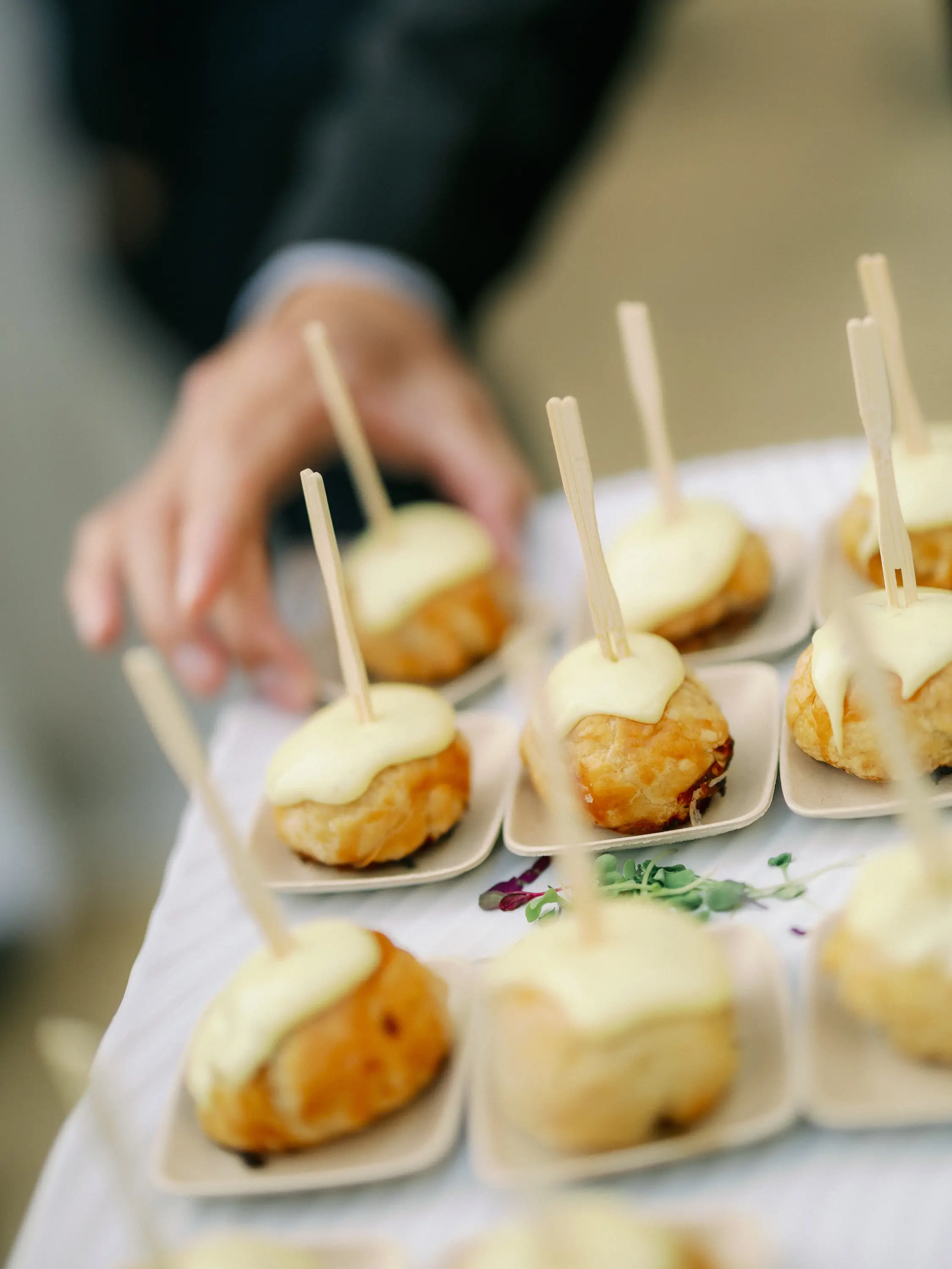 Mini puff pastry appetizers with creamy sauce on top, served on small plates with wooden picks.