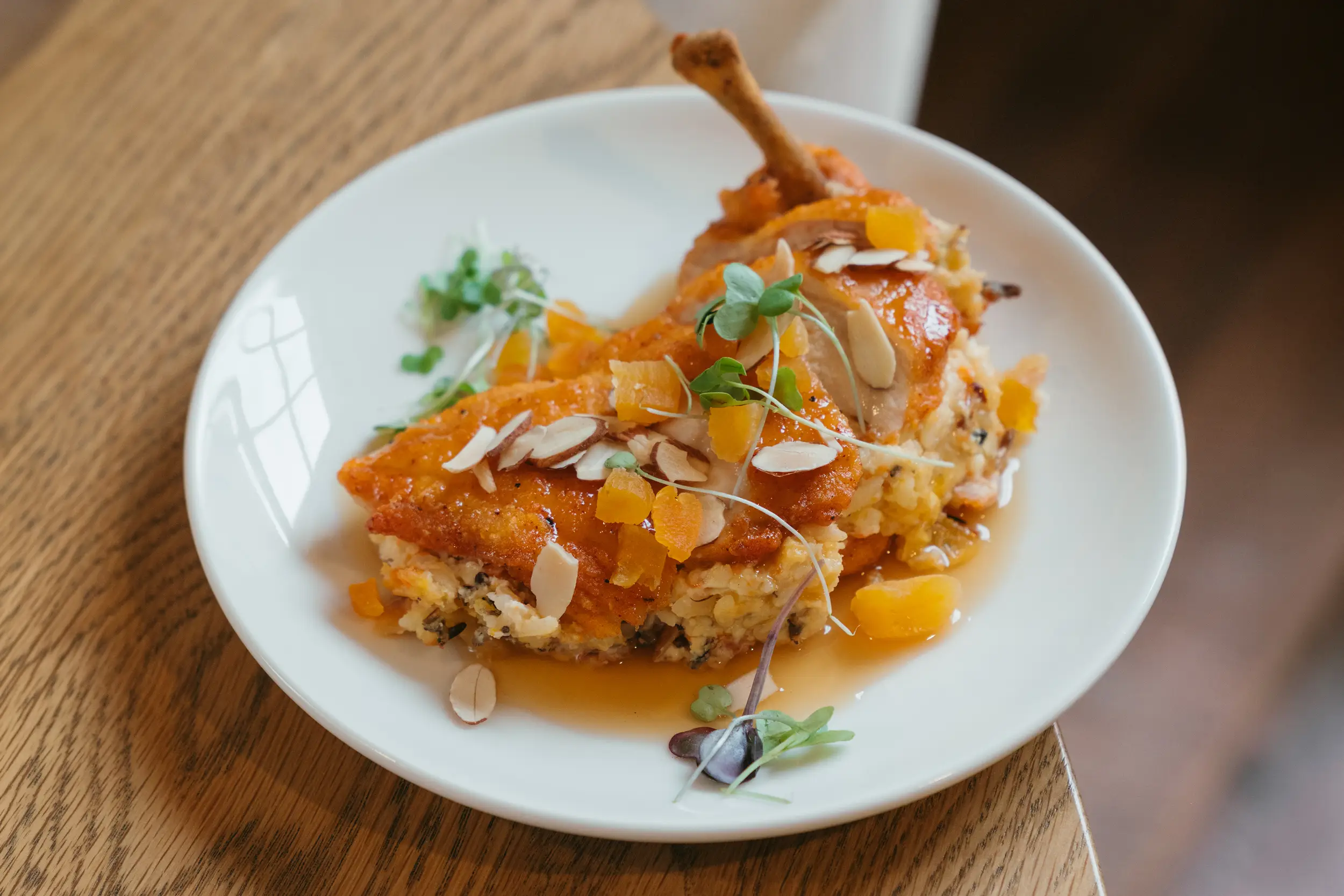 Plated gourmet chicken dish garnished with sliced almonds, microgreens, and diced orange pieces on a white plate.