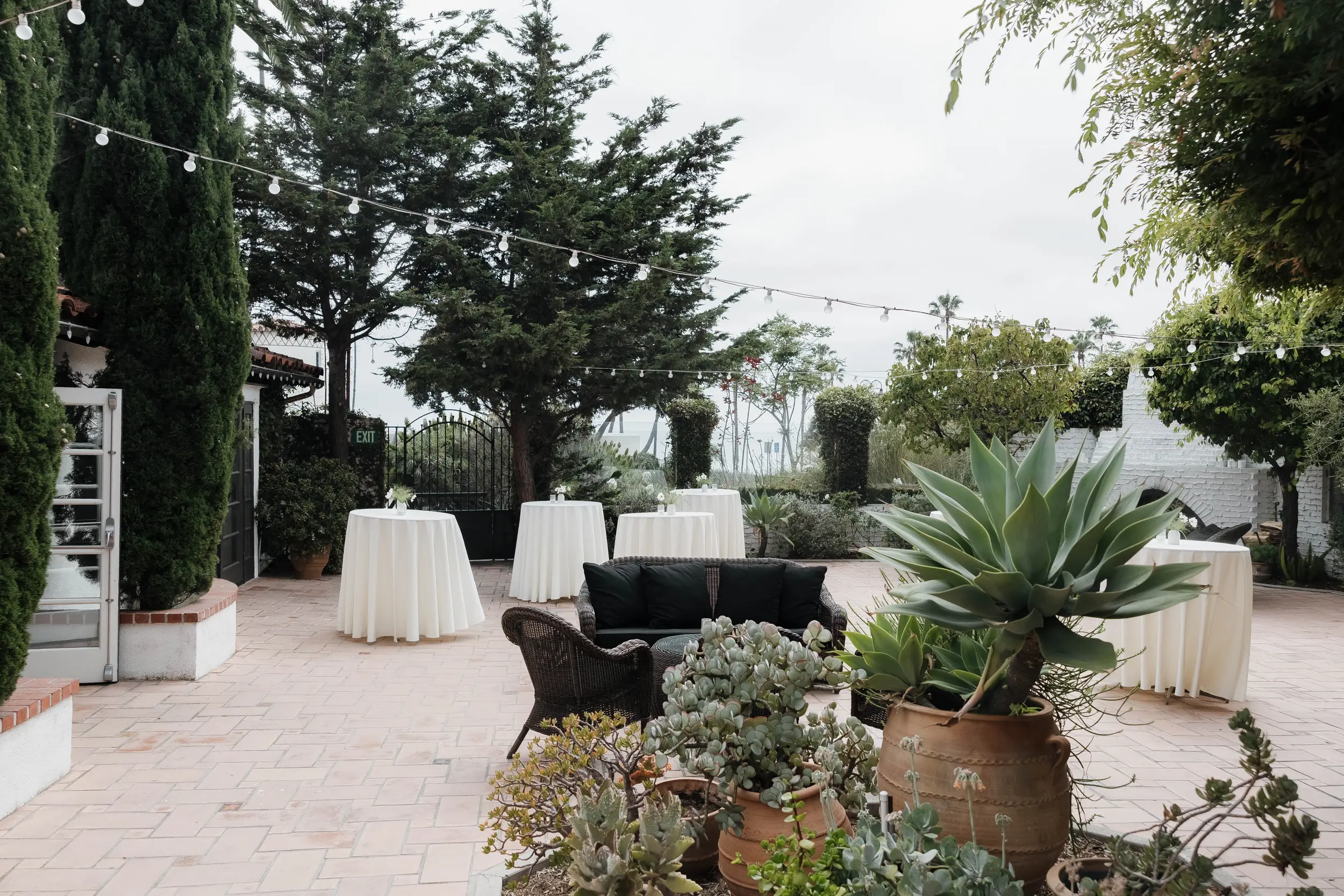 Cocktail tables draped in ivory linens are scattered across the Patio of the Stars for cocktail hour. You can see the ocean peeking through in the distance.