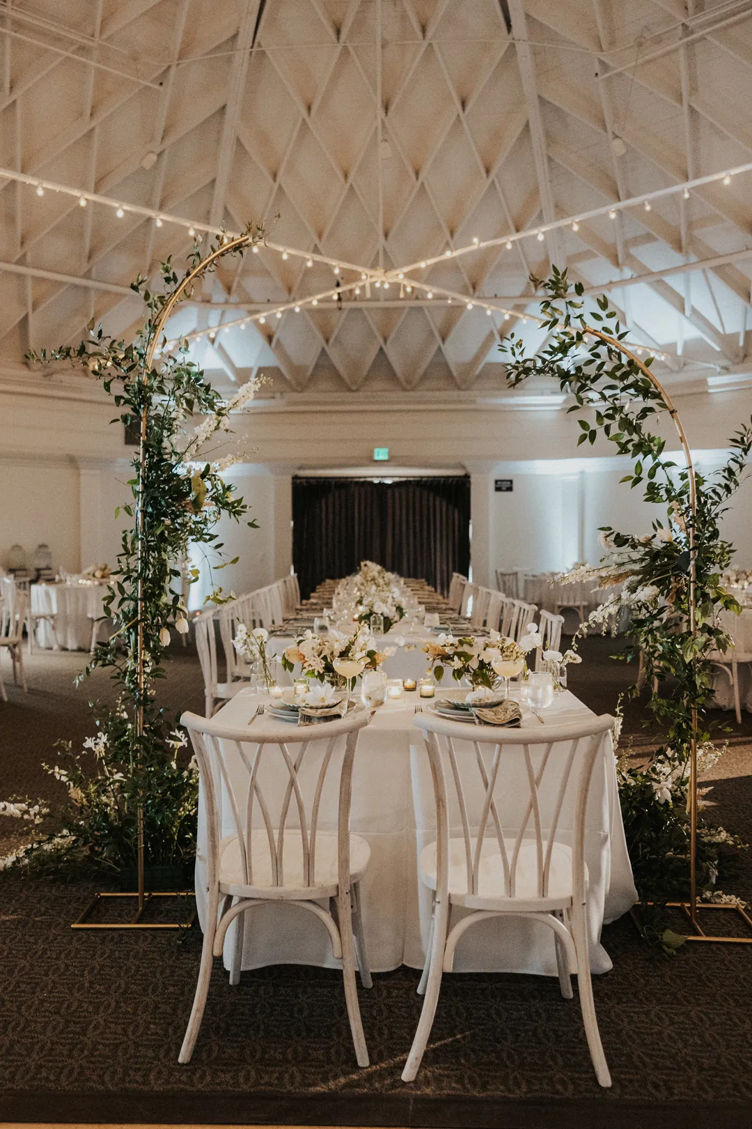 The sweetheart table is framed in by greenery and faces all the other reception tables in the ballroom.