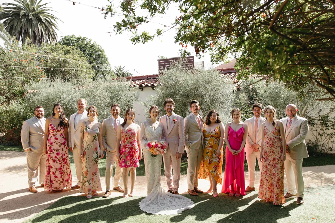 Bridesmaids dressed in pink and orange and groomsmen dressed in tan stand with the bride and groom for wedding party group photos.
