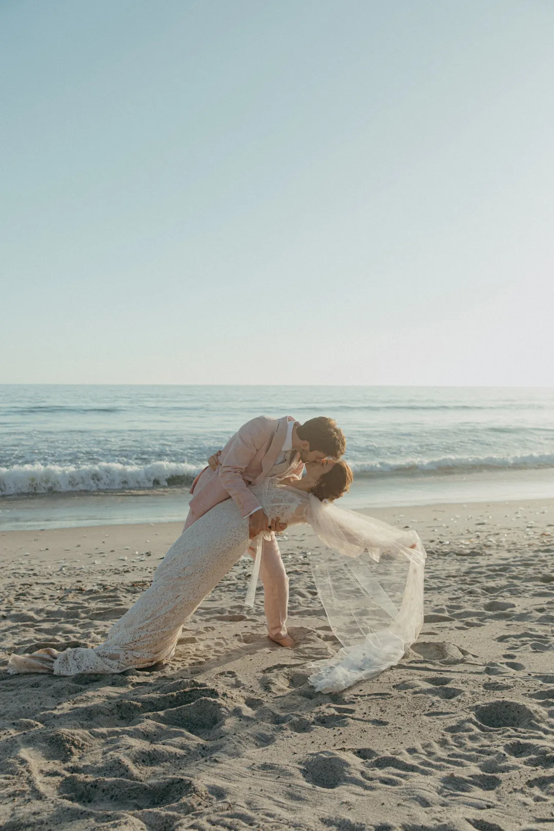Bride and groom share a kiss on the beach.