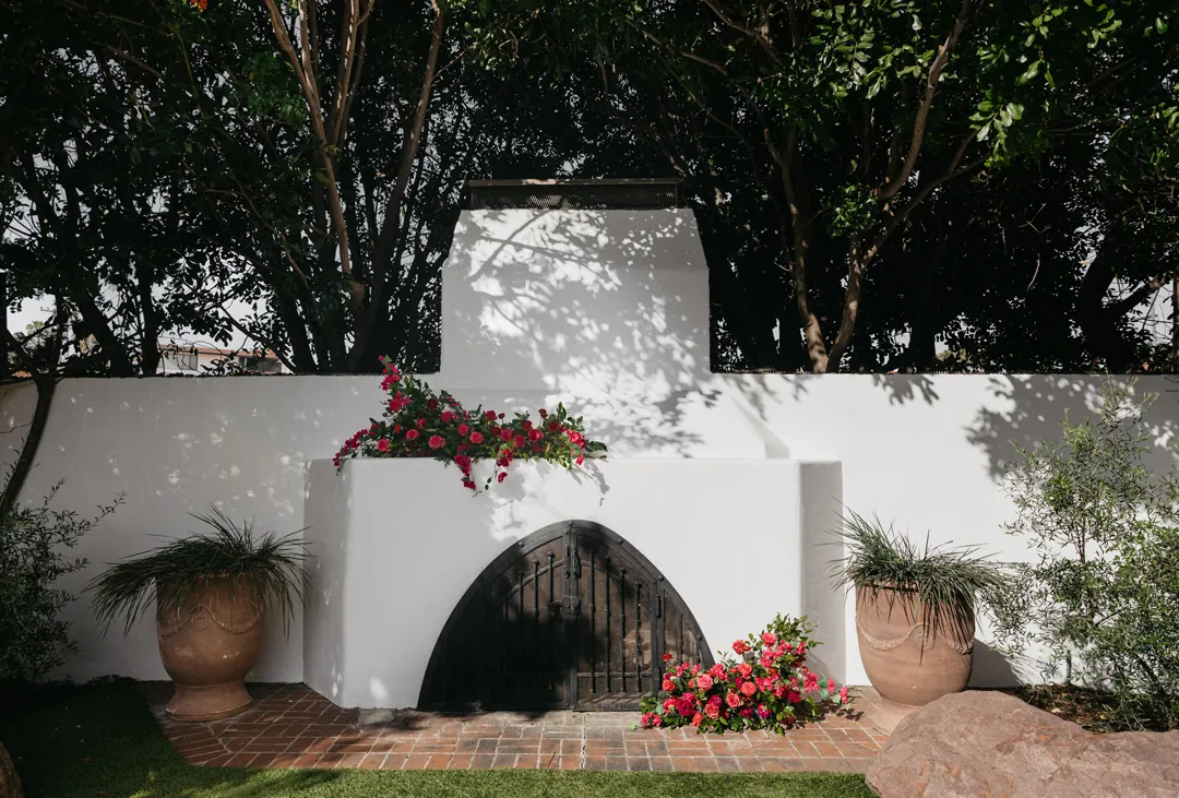 Pink floral wedding ceremony decor tops an outdoor fireplace mantle.