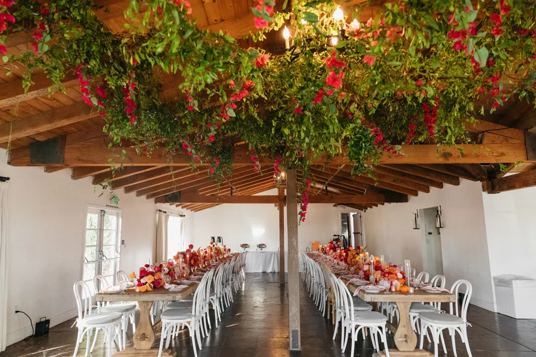 Vibrant flowers top reception tables and hang from the wooden rafters for a summertime wedding reception at The Casino San Clemente.
