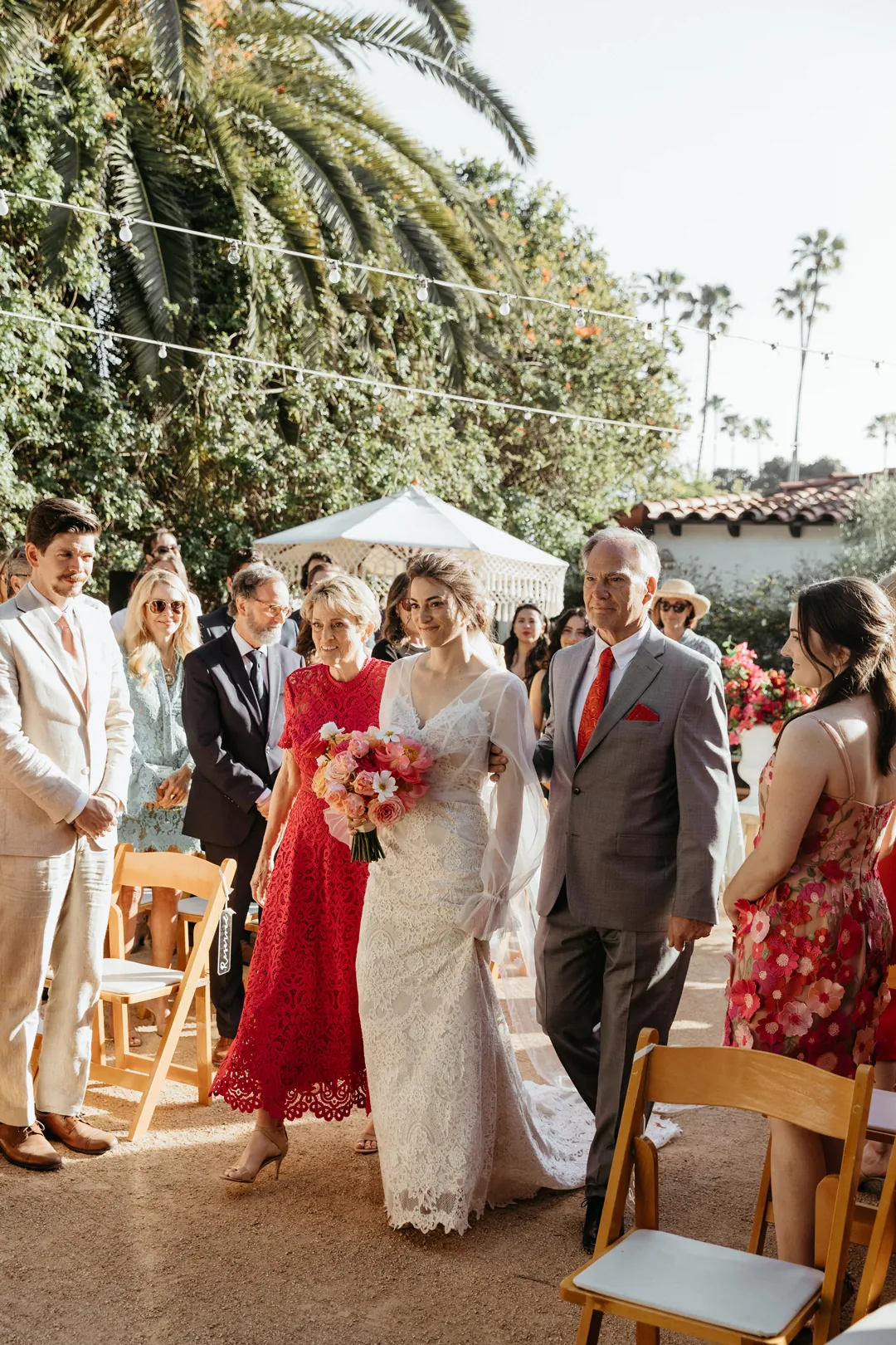 Bride walks down the aisle arm-in-arm with her parents.