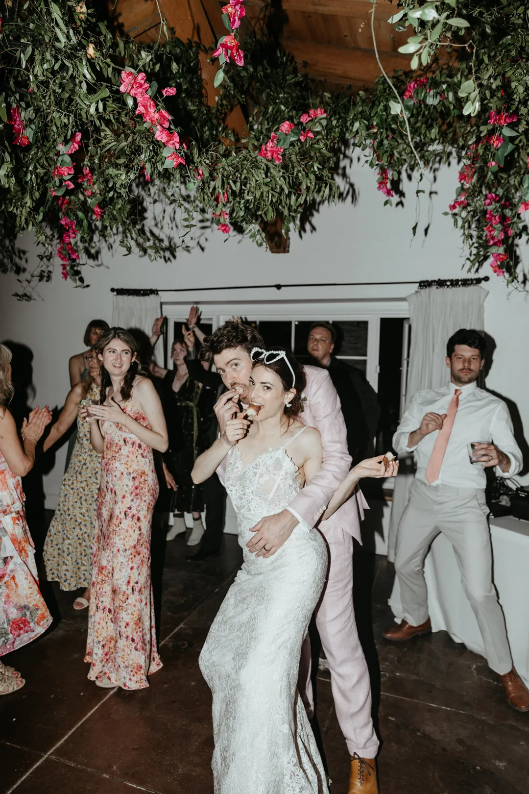 Bride and groom eat a donut while sharing a dance out on the dance floor.