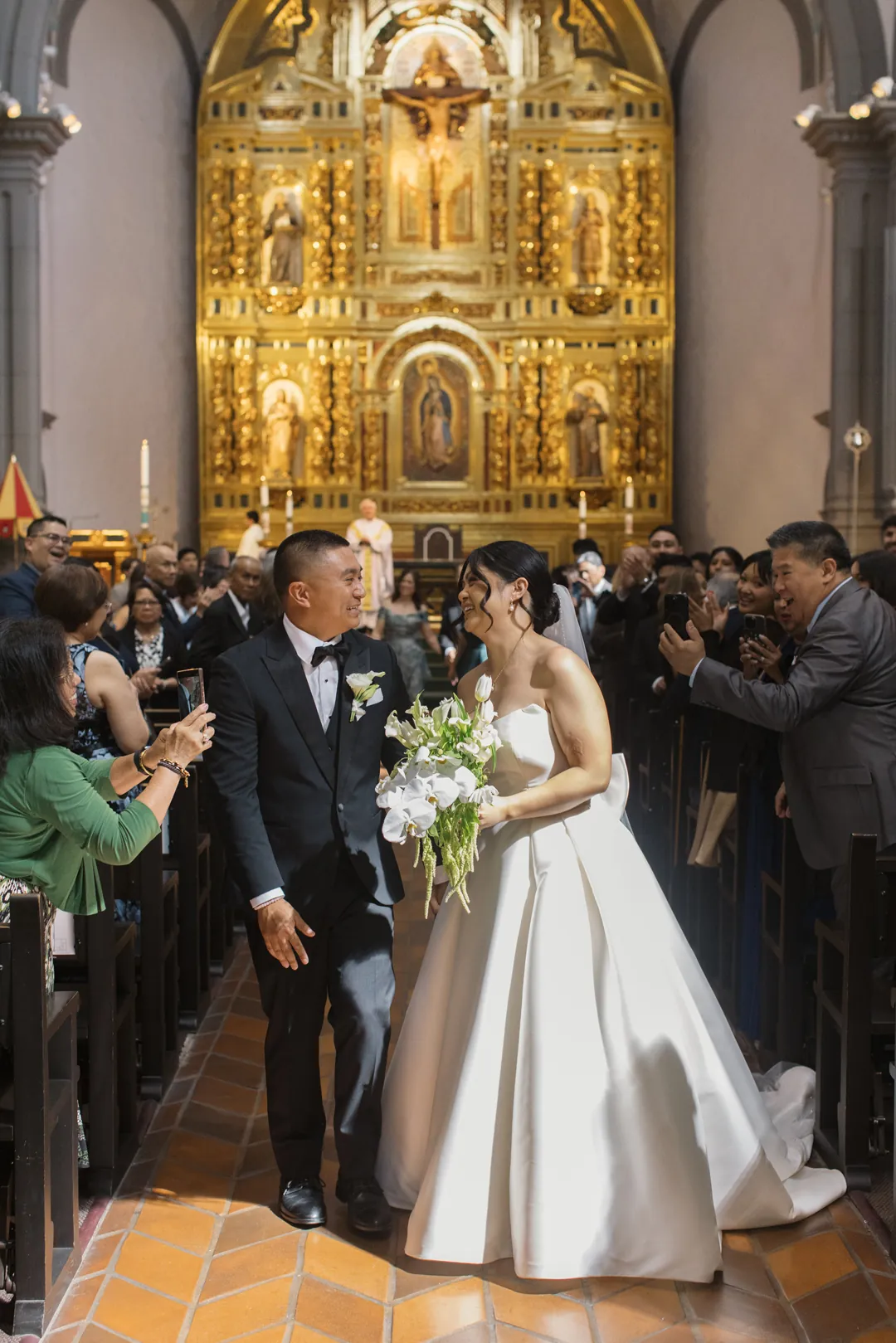 bride and groom exit their ceremony as guests cheer from their seats.