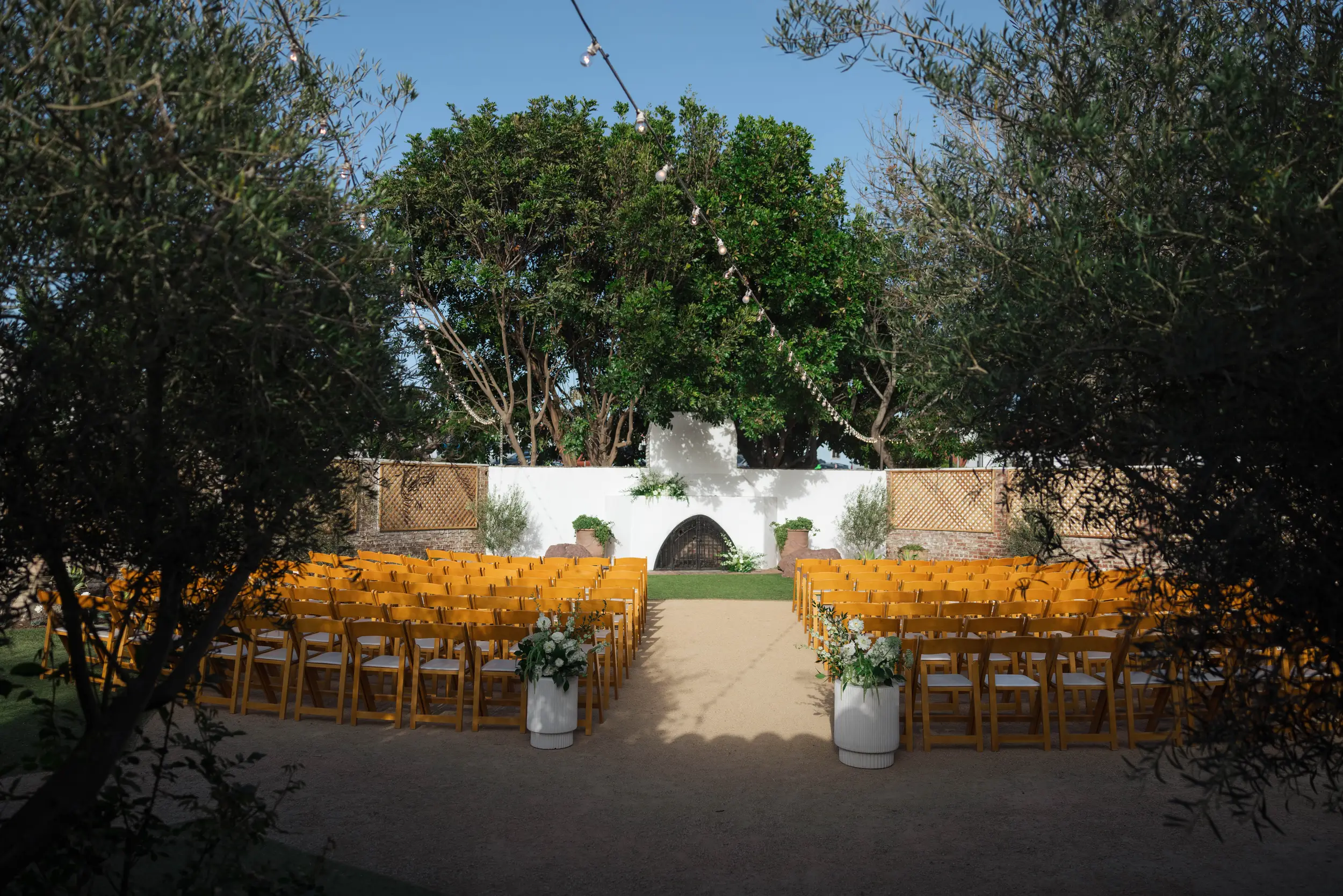 Rows of wooden ceremony chairs and white aisle flowers in the tree-lined Rock Garden.