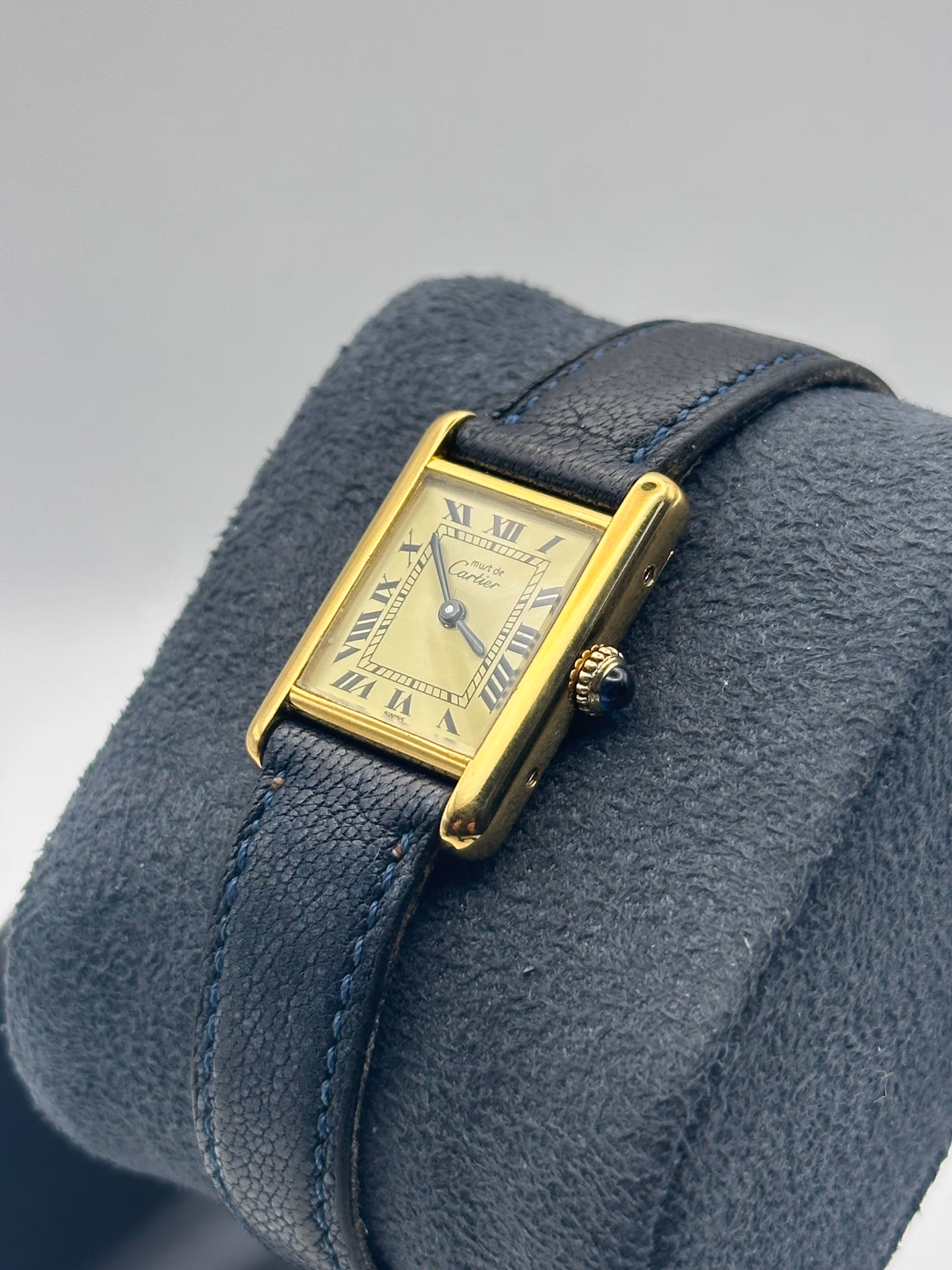 Élégante et intemporelle, cette Tank Must de Cartier datant de 1979 incarne parfaitement le raffinement emblématique de la maison. Son boîtier de 20 mm en vermeil plaqué or lui confère une présence discrète et sophistiquée au poignet, tandis que son cadran champagne orné de chiffres romains renforce son allure classique et chaleureuse. Animée par un mouvement à remontage manuel, elle a été entièrement révisée en 2026, garantissant un fonctionnement optimal. Cette pièce est accompagnée de sa boîte et de ses papiers d’origine, et se distingue par un bracelet bleu élégant associé à une boucle Cartier, apportant une touche de contraste moderne à ce modèle vintage d’exception.