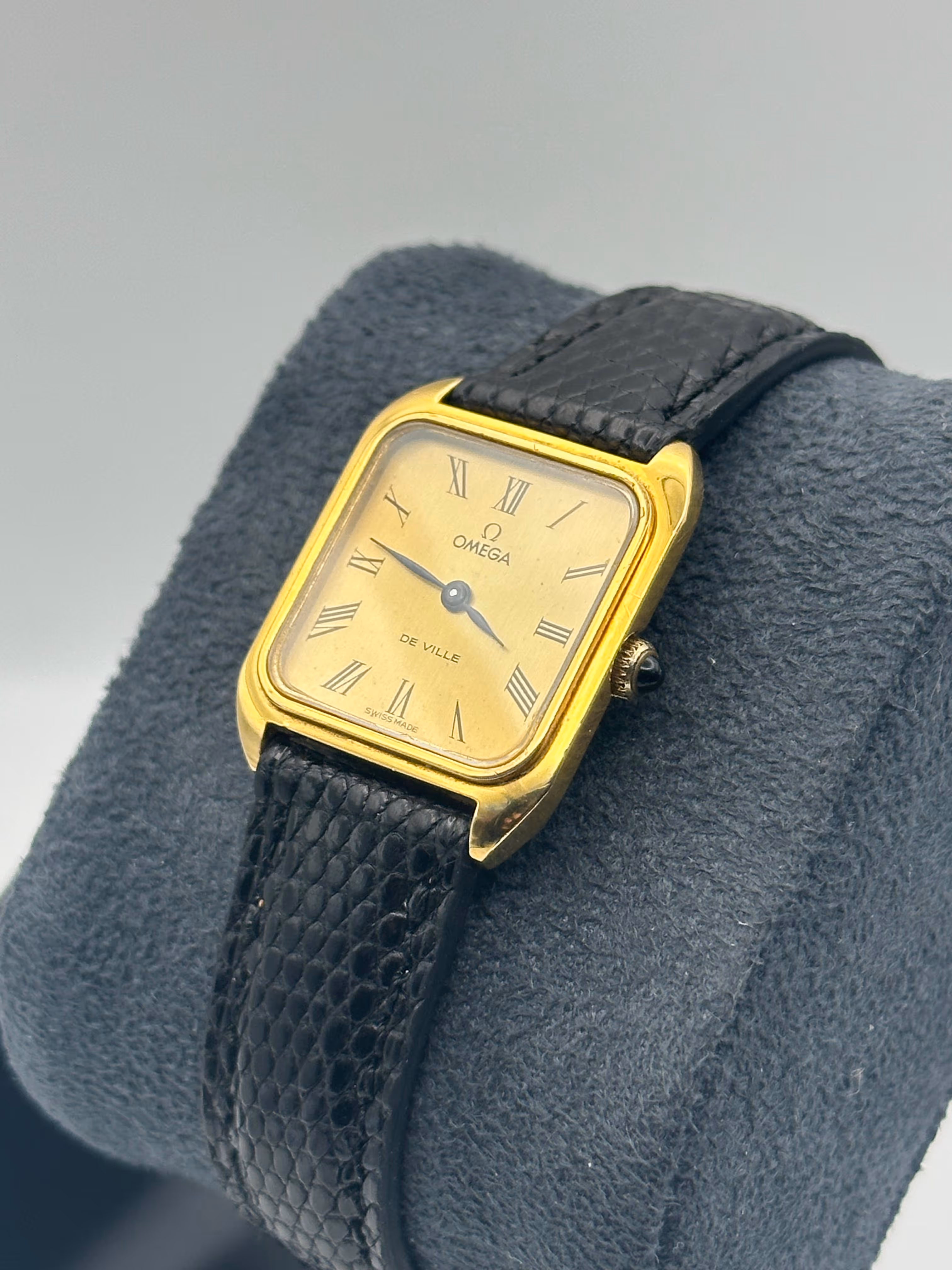 Élégante et résolument vintage, cette Omega De Ville séduit par son boîtier carré de 23 mm couleur or, offrant une silhouette à la fois discrète et raffinée. Son cadran champagne, sublimé par des chiffres romains, apporte une touche de chaleur et de sophistication tout en renforçant son esthétique classique et intemporelle. Animée par un mouvement à remontage manuel, elle incarne le charme des montres traditionnelles, où chaque geste participe à l’expérience. Elle est montée sur un bracelet sur mesure en lézard noir brillant, qui souligne son caractère distingué et complète harmonieusement cette pièce au style sobre et élégant.