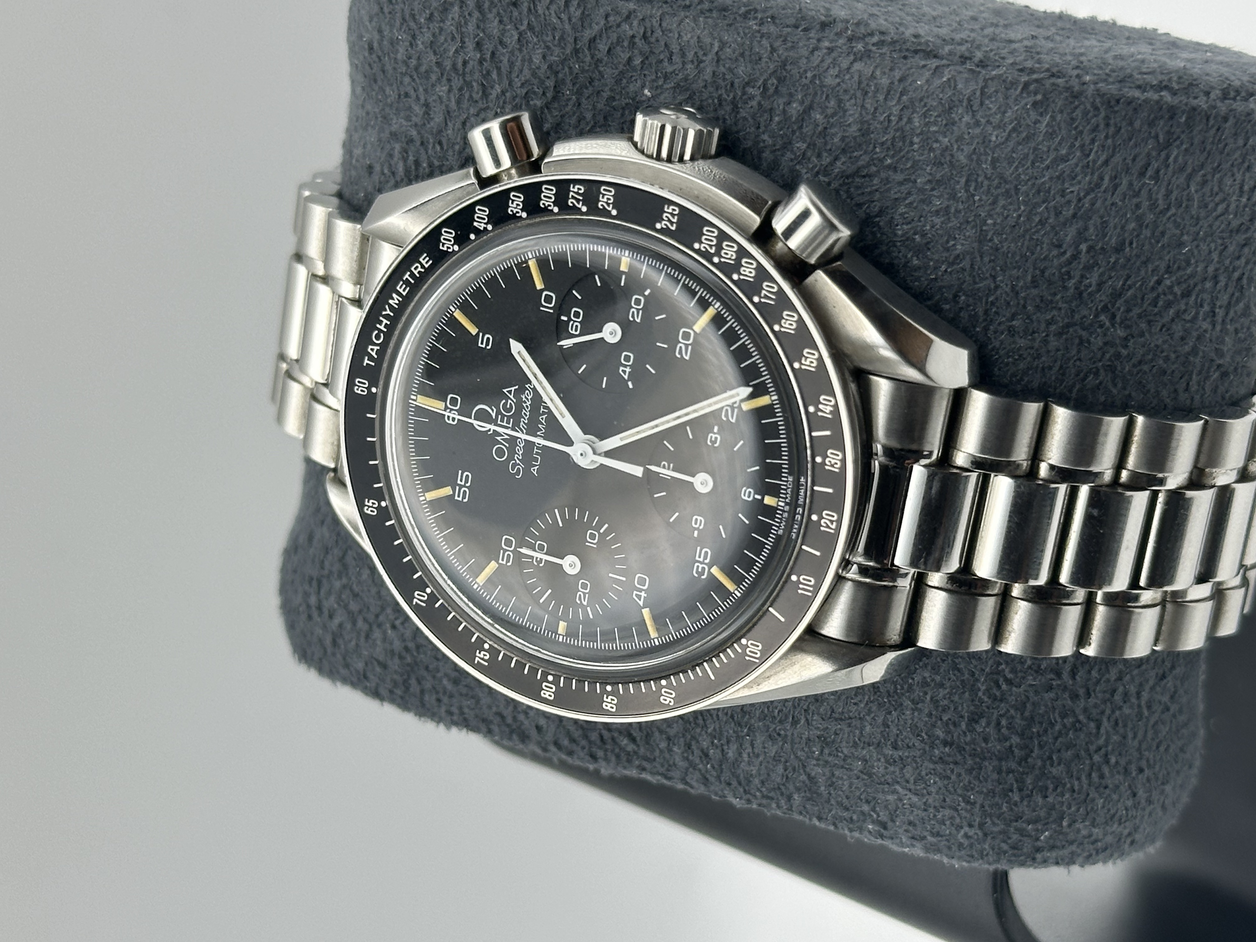 Une véritable capsule temporelle datant de 1996. Cette Omega Speedmaster Reduced est proposée avec sa boîte et ses papiers d’origine. Elle se trouve dans un état remarquable, proche du neuf, n’ayant jamais été portée. Offerte à l’origine par une entreprise à son propriétaire pour récompenser 25 années de service fidèle et gravée pour l'occasion, la montre a été soigneusement conservée depuis. Au fil du temps, les index ont développé une magnifique patine, apportant chaleur et caractère à l’ensemble tout en préservant le charme authentique et l’originalité de la montre.