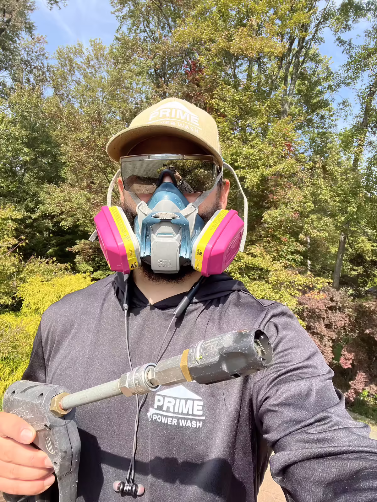 Person wearing a Prime Power Wash cap and shirt with a protective mask and goggles, holding a pressure washer wand.