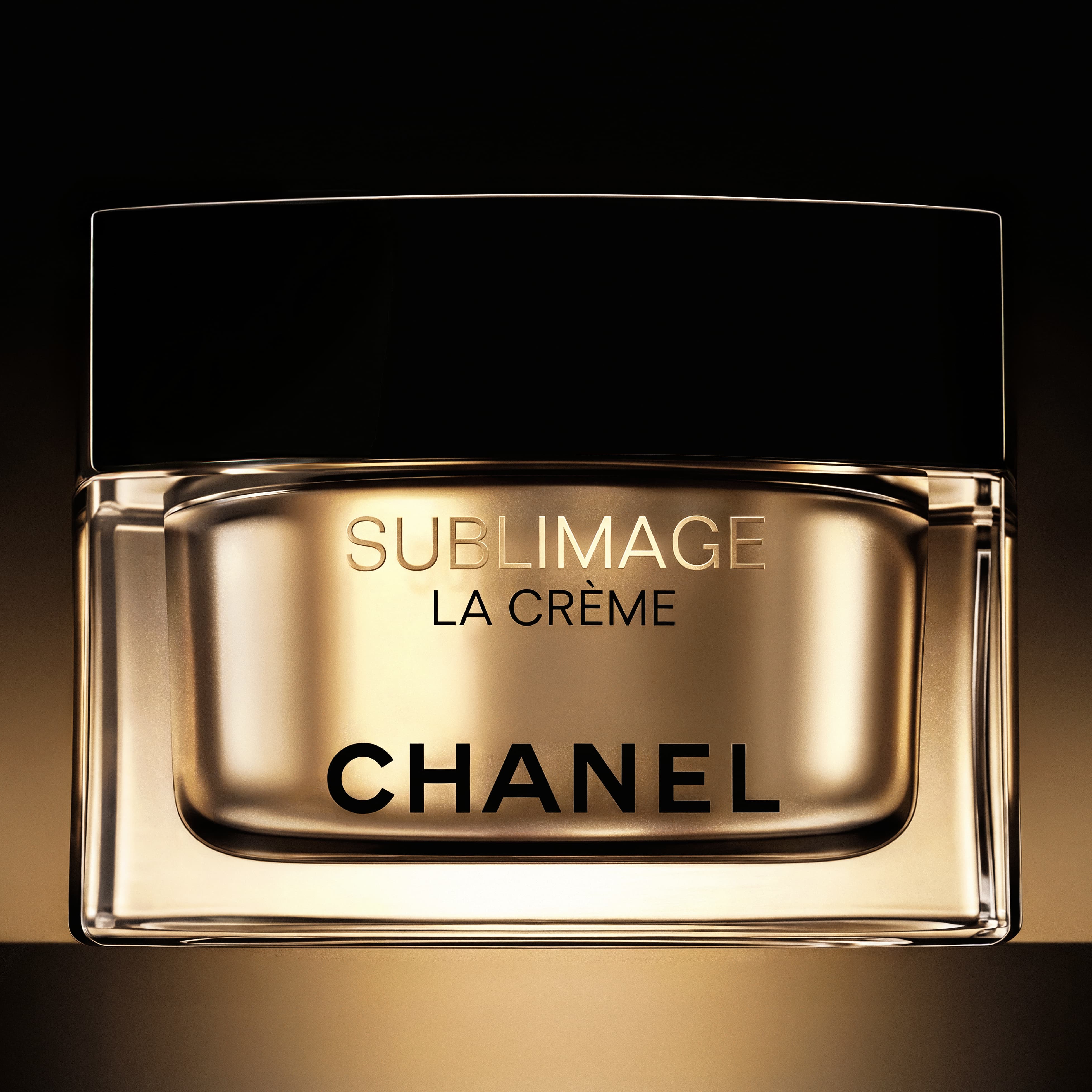 Close-up of a gold-toned Chanel Sublimage La Crème jar with a black lid against a dark gradient background.