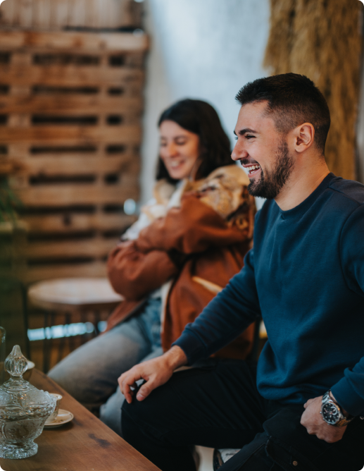 Man laughing and woman smiling while in a cozy indoor setting.