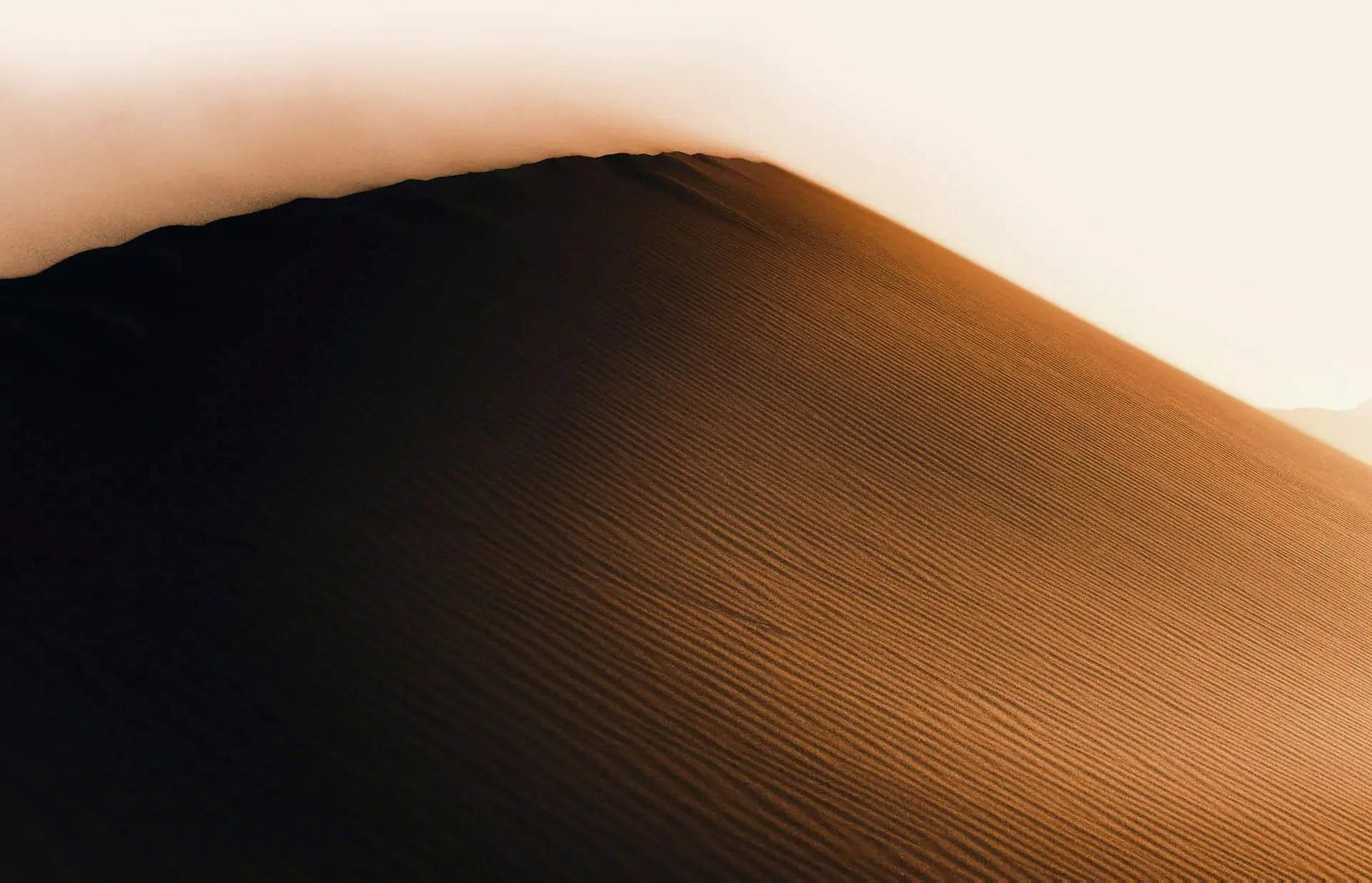 Wide angle shot of a desert dune with wind blown sand on the ridge