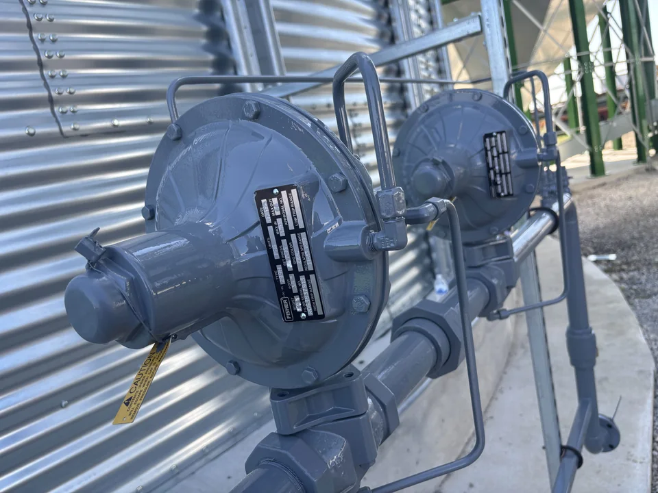 Twin natural gas regulators mounted on piping along the corrugated steel wall of a grain bin.