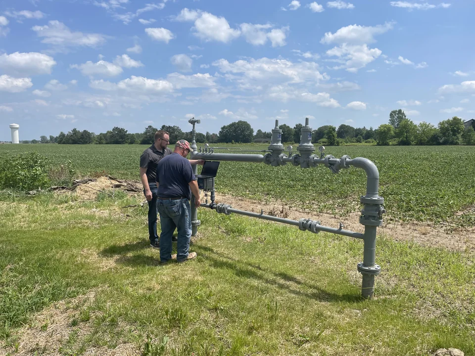 District regulator station installed at the edge of a farm field, with two technicians on site.