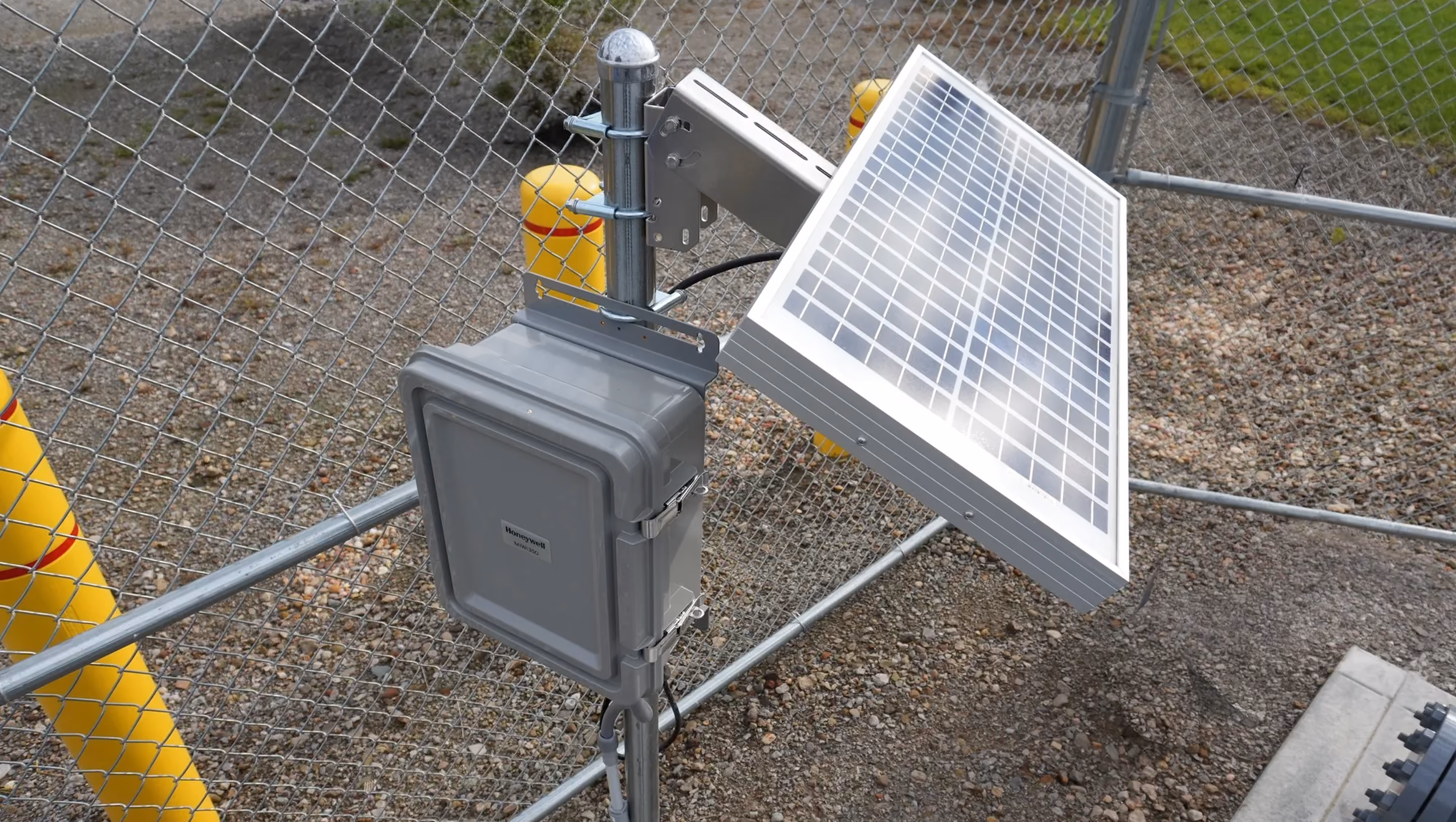 Honeywell MIWI communications enclosure with a solar panel, post-mounted at a fenced gas station.