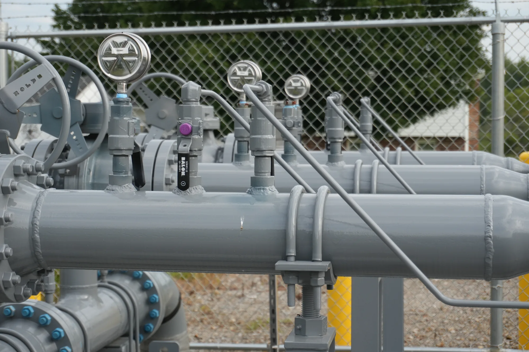 Row of pressure gauges and instrument taps welded along a natural gas manifold header at a fenced station.