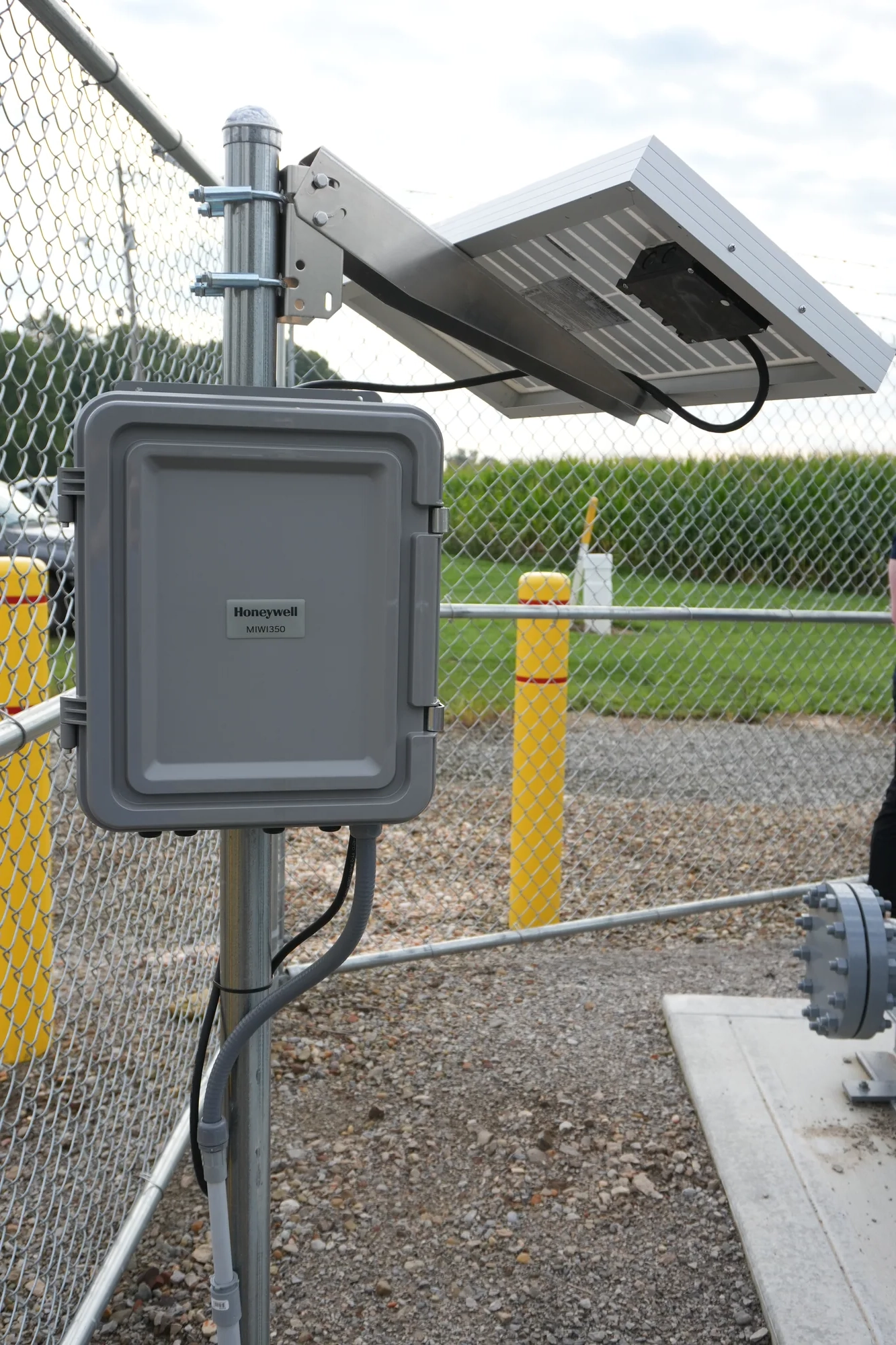 Honeywell MIWI350 telemetry enclosure and solar panel mounted on a fence post beside a cornfield.