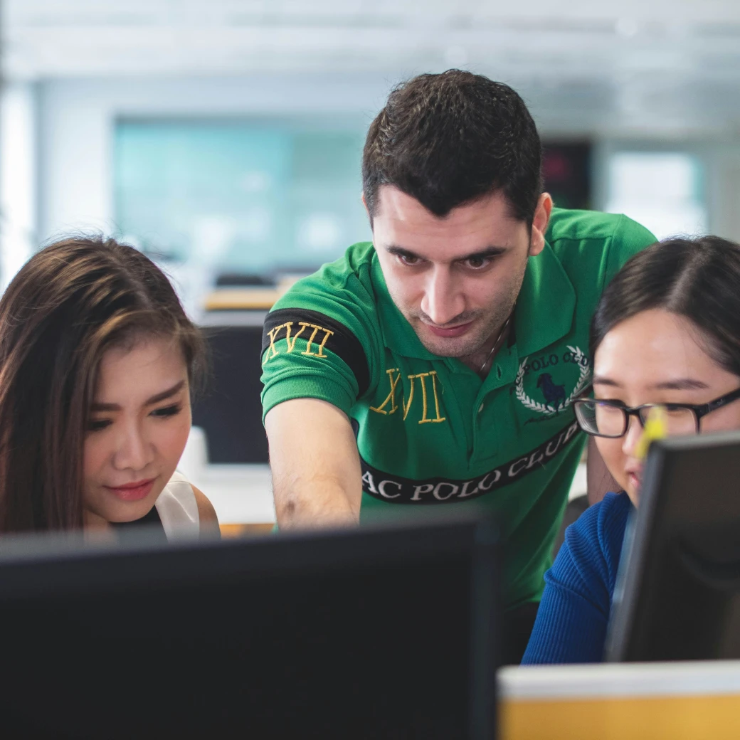 Man in green polo shirt explaining work to colleagues at a computer