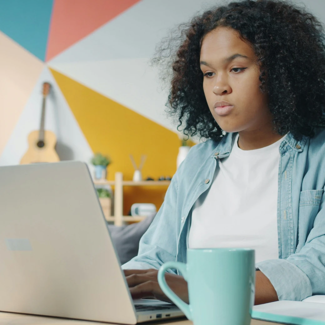 Young woman with curly hair focused on typing on a laptop at work