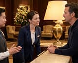 Businesswoman in a navy suit listening attentively to two men engaged in conversation in a warmly lit indoor setting.