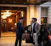 Hotel doorman helping a well-dressed man with his luggage outside a luxury hotel entrance.