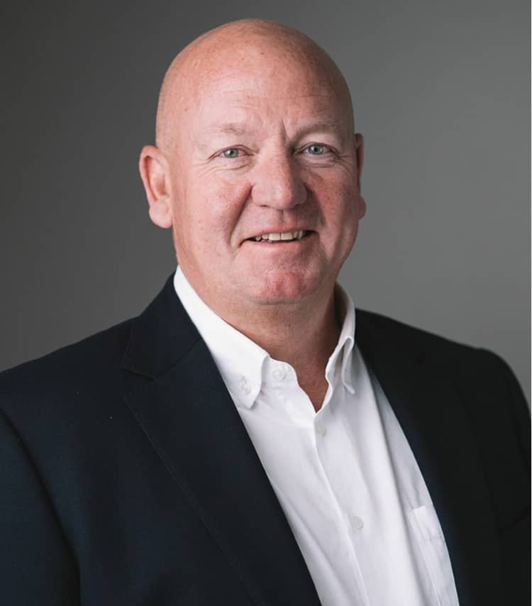 Smiling bald man wearing a white shirt and black blazer against a gray background.