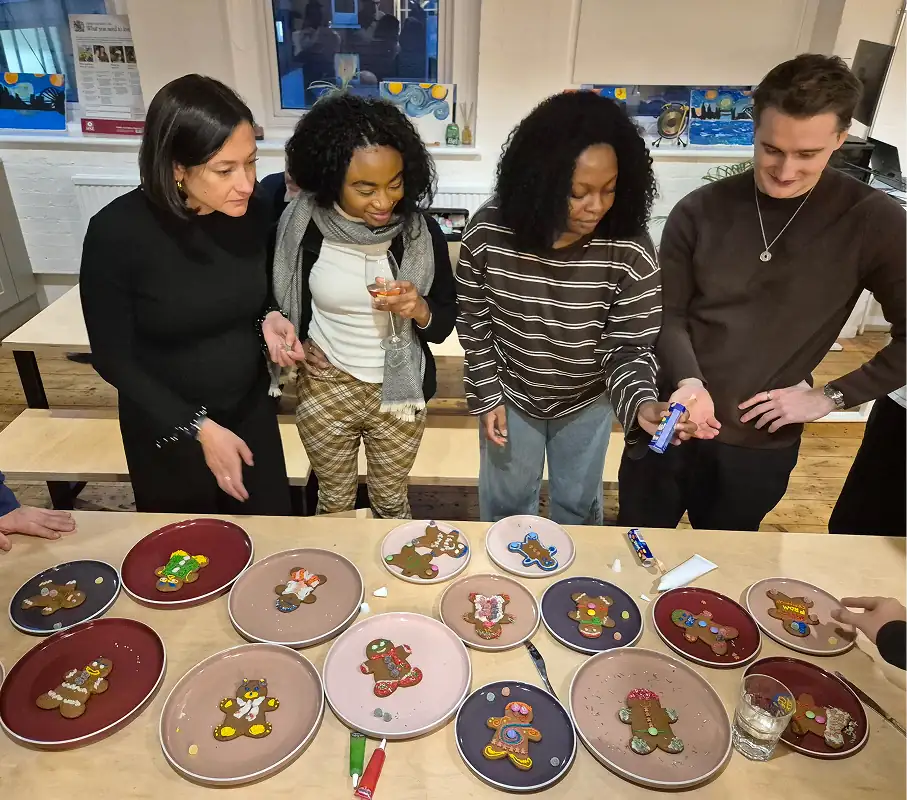 Four adults looking at decorative plates with holiday gingerbread designs on table