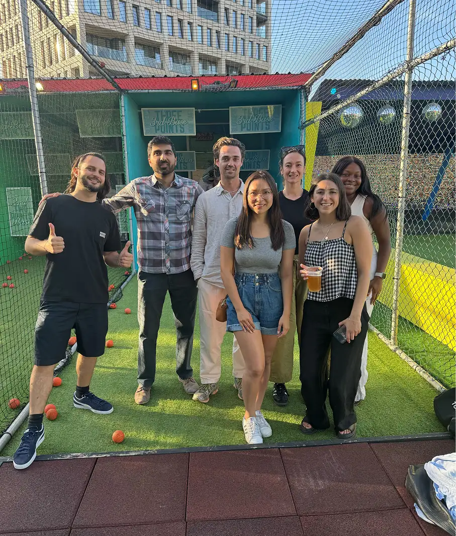 Group of seven people posing together at an indoor golf or sports facility with green turf.