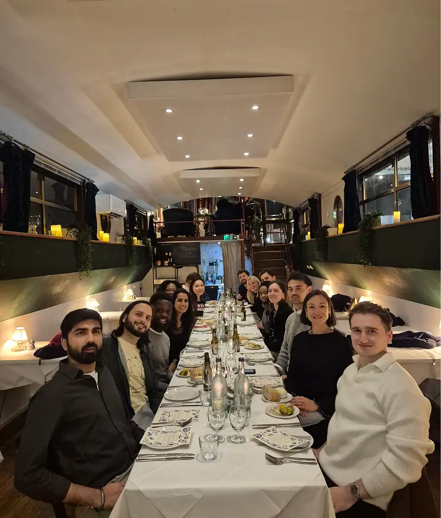 Group of people dining at a long table inside an elegant luxury bus or mobile venue