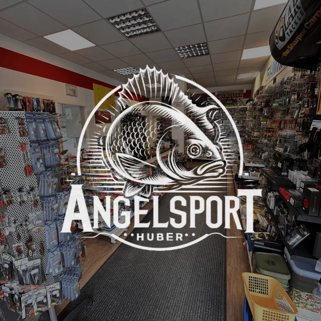 Innenansicht eines Angelgeschäfts mit Angelzubehör an Wänden und Regalen sowie dem Logo Angelsport Huber mit einem Fisch in der Mitte.