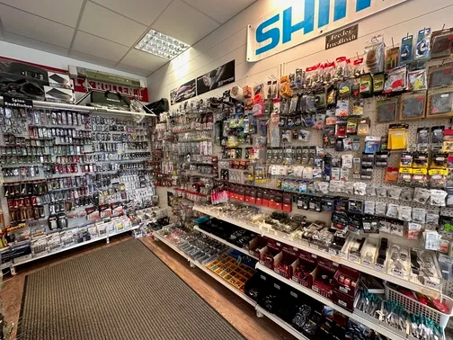 Ein Laden mit Wänden voller Angelzubehör und Zubehörsets, darunter Haken, Schnüre und Köder, gut organisiert an Regalen und Haken.
